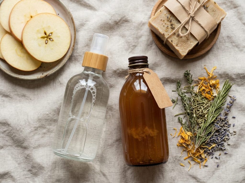 Natural Answer Products soap bars and tooth powder jars arranged on a wooden surface with green botanicals nearby.